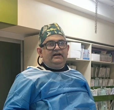 دکتر رادنوش پشم فروش، فوق تخصص اینترونشنال نورورادیولوژی، با گان آبی و کلاه جراحی؛ پشت سر او قفسه‌های جعبه‌های تجهیزات پزشکی دیده می‌شود
